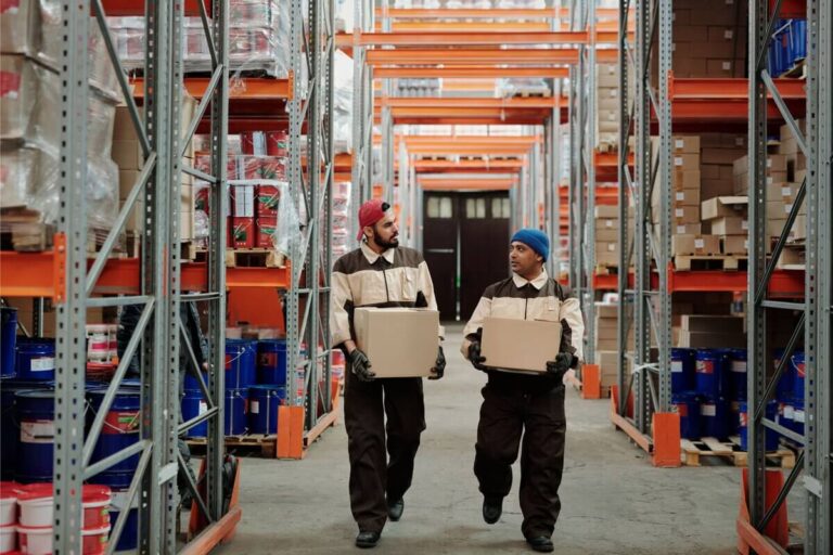 Warehouse workers carrying boxes in a fulfillment center aisle
