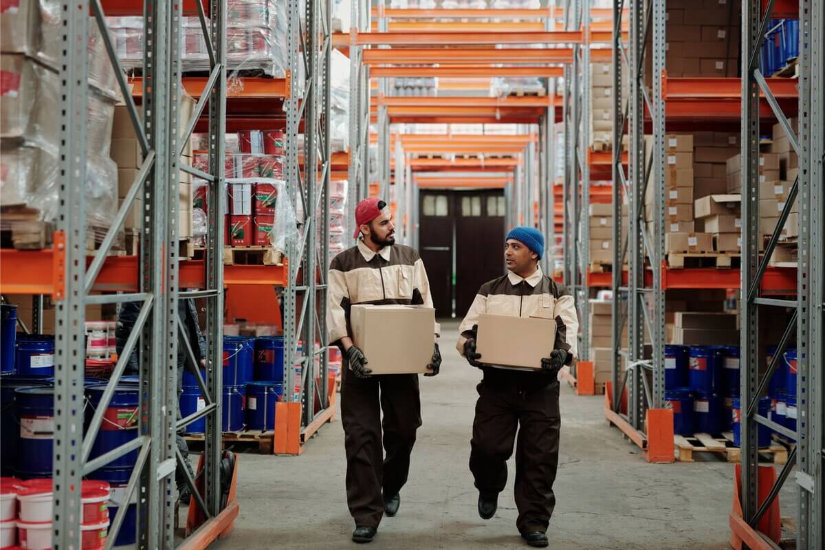 Warehouse workers carrying boxes in a fulfillment center aisle